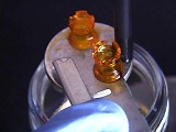 2 small, orange 3D Prints sitting on razor blade