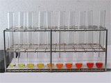 several glass test tubes in rack holding small amounts of liquid ranging form clear on the left through shade of yellow to dark orange and red on the right.