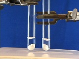 two test tube held by clamps, holding small amount of clear liquid with white substance settled on bottom