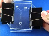 PDMS Fluidics experimental set up using binder clips holding both end of film with dots of clear substance on top.