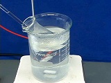 glass stir rod inside glass test tube that is sitting in 250mL glass beaker with red and white wires submerged in clear liquid