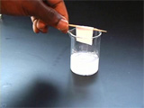 PMMA Diffraction, hand holding toothpick with small paper taped to it, on top of 20 mL beaker
