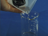 hand pour clear liquid from small plastic weighboat into empty 50 mL beaker