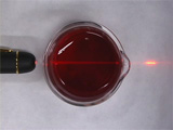 looking into small glass beaker filled with red liquid with red laser pointer shining through it left to right