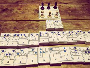 A picture of the hexapawn game showing the three by three grid game board with 3 black pieces on one side and 3 white pieces on the other.  There are cards showing several possible permutations of the way the pieces can move in the game. 